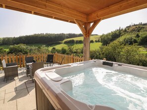 A hot tub with a wooden deck and chairs, overlooking a green landscape. - Ploony Hill Cabin (Knighton)