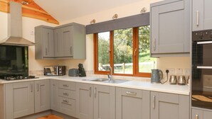 A modern kitchen with grey cabinets, a stainless steel range hood, a built-in oven, and a window with a view of greenery.