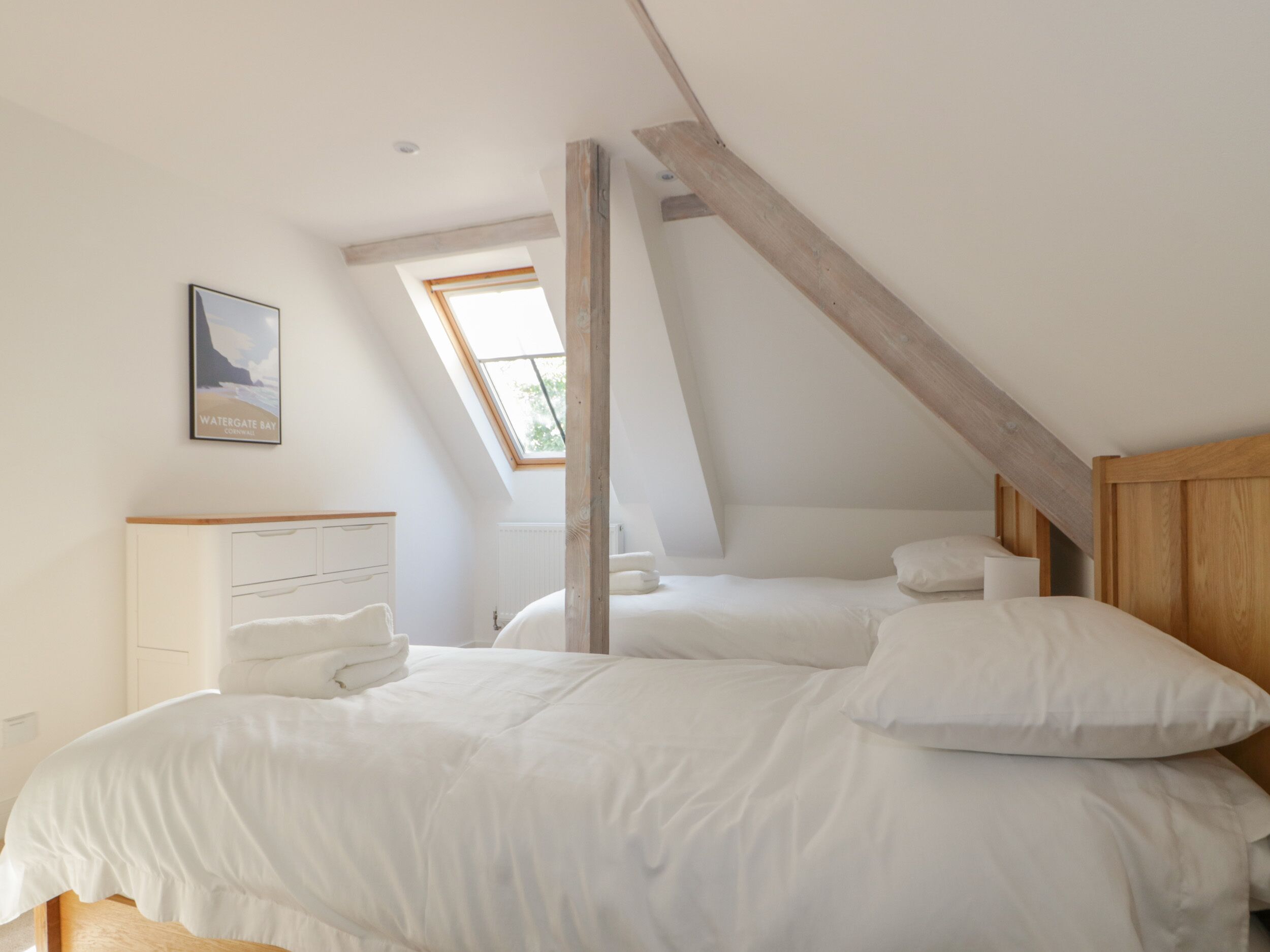 A bedroom with a sloped ceiling, a skylight, a bed with white bedding, a bedside table, and a framed picture on the wall.
