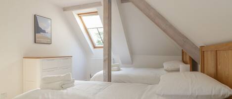 A bedroom with a sloped ceiling, a skylight, a bed with white bedding, a bedside table, and a framed picture on the wall.