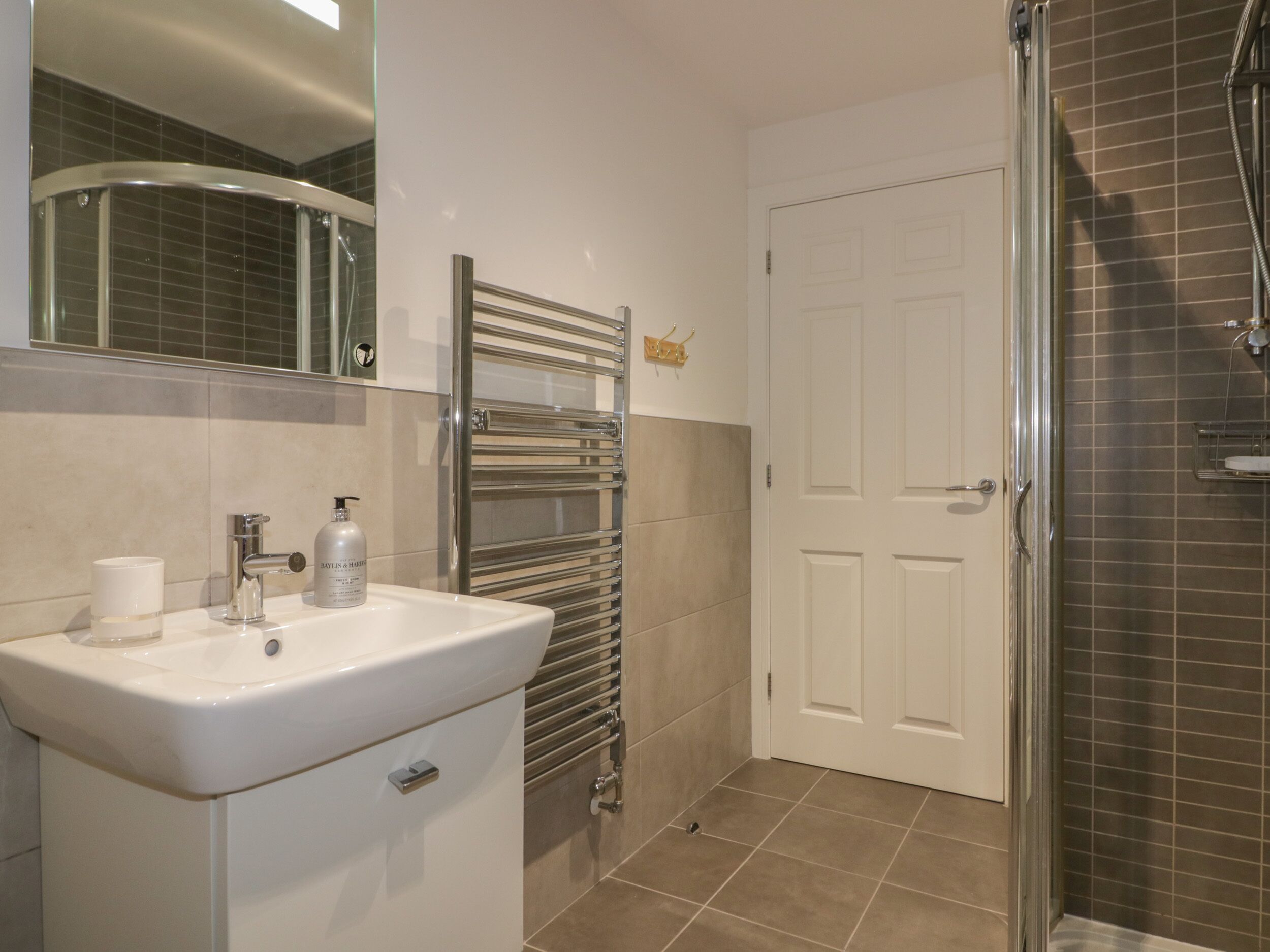 Een badkamer met een witte wastafel, een spiegel, een handdoekhouder en een douche.