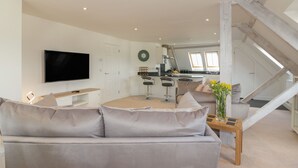 Una sala de estar moderna con un sofá gris, un televisor de pantalla plana y un comedor con taburetes de bar.
