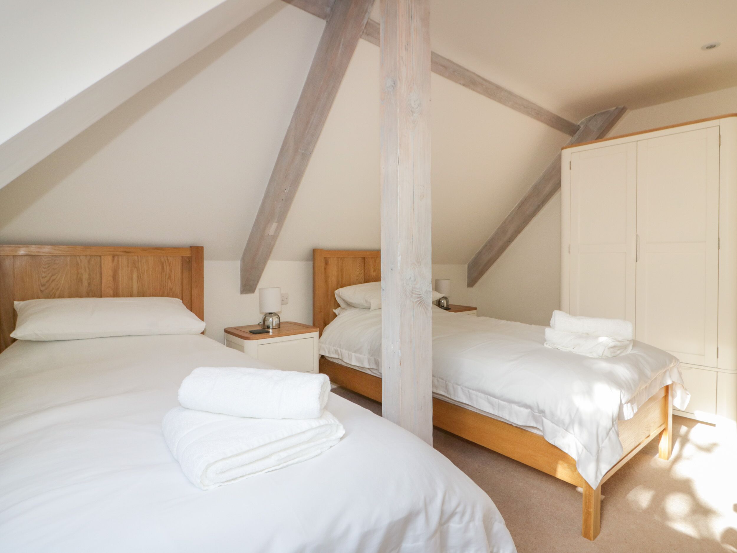 Ein Schlafzimmer mit zwei Betten, Holz-Kopfteilen, weißer Bettwäsche und einem Kleiderschrank.