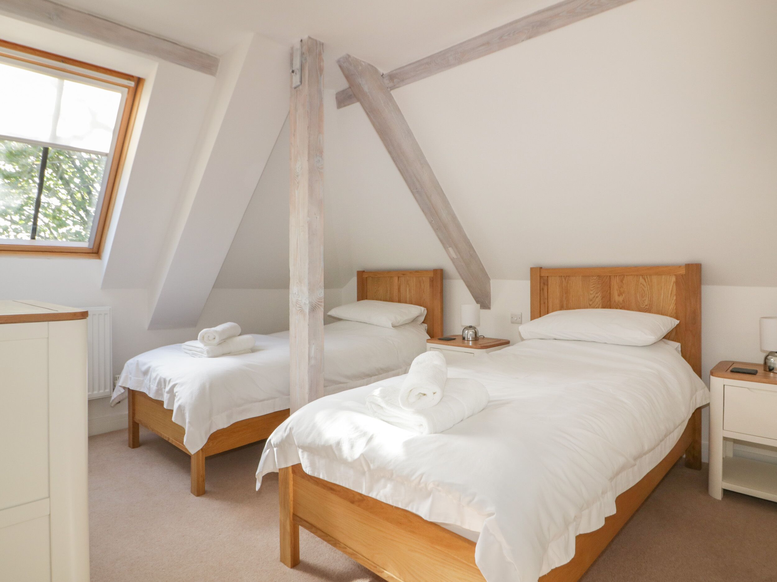 A bedroom with two wooden beds, white bedding, and a sloped ceiling.