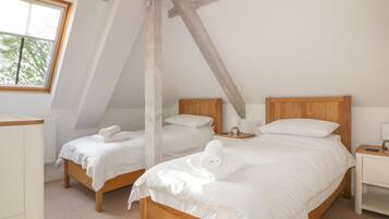A bedroom with two wooden beds, white bedding, and a sloped ceiling.