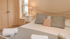 Una cama bien hecha con una manta gris, almohadas blancas y una mesita de noche con una lámpara.