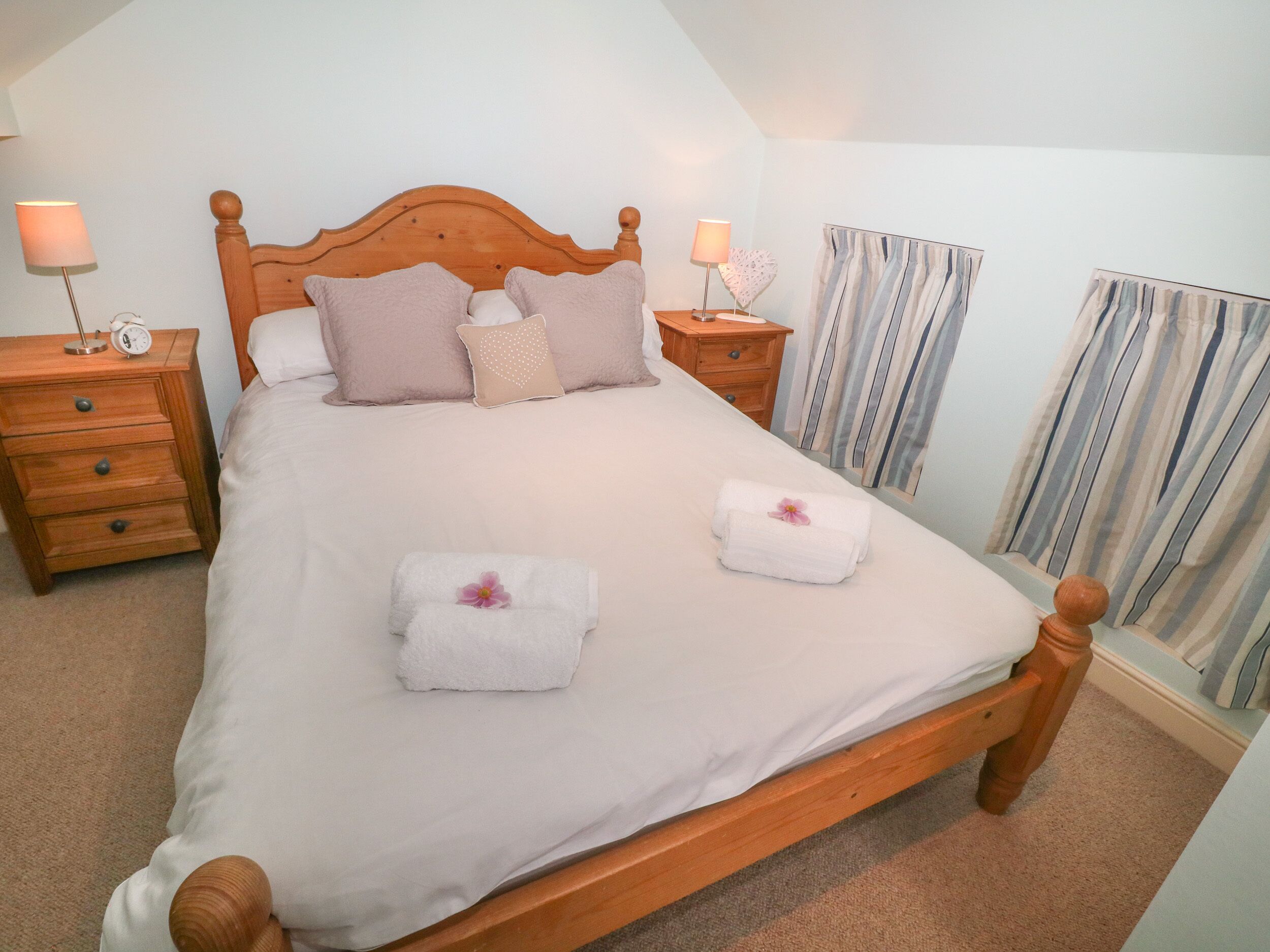 A neatly made bed with two towels, a wooden headboard, two bedside tables with lamps, and striped curtains.