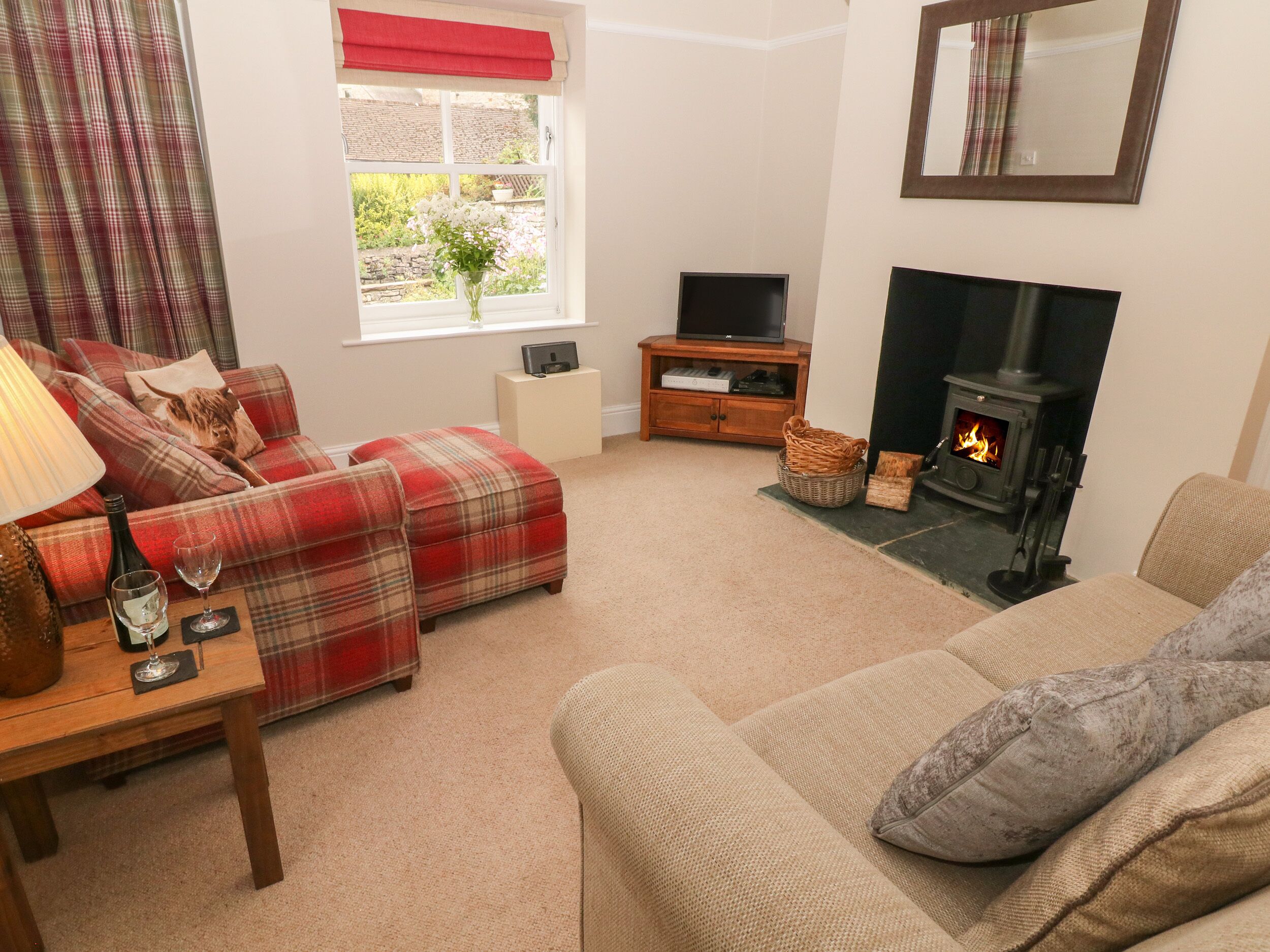 A cozy living room with a sofa, ottoman, and a television on a wooden stand. A fireplace is visible in the background.