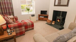 Una sala de estar acogedora con un sofá, un reposapiés y un televisor sobre un mueble de madera. Se ve una chimenea al fondo.