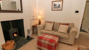Una sala de estar acogedora con chimenea, un sofá, un reposapiés y una lámpara.