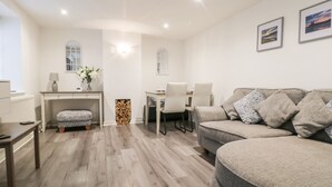 A modern living room with a grey sofa, a small table, a bench, and a fireplace. - Swallow Cottage (Herne Bay)