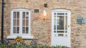 A brick building with two windows and a door, a sign for Swallow Cottage, and a lamp on the wall. - Swallow Cottage (Herne Bay)
