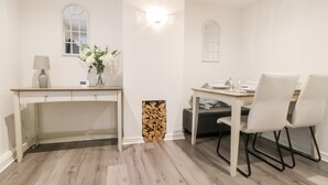 A modern kitchen with white cabinetry, a wooden countertop, and a dining area with a table and chairs. - Swallow Cottage (Herne Bay)