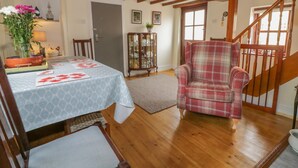 Un salon chaleureux avec un plancher en bois, un fauteuil à carreaux, une table à manger recouverte d’une nappe bleue et un escalier.