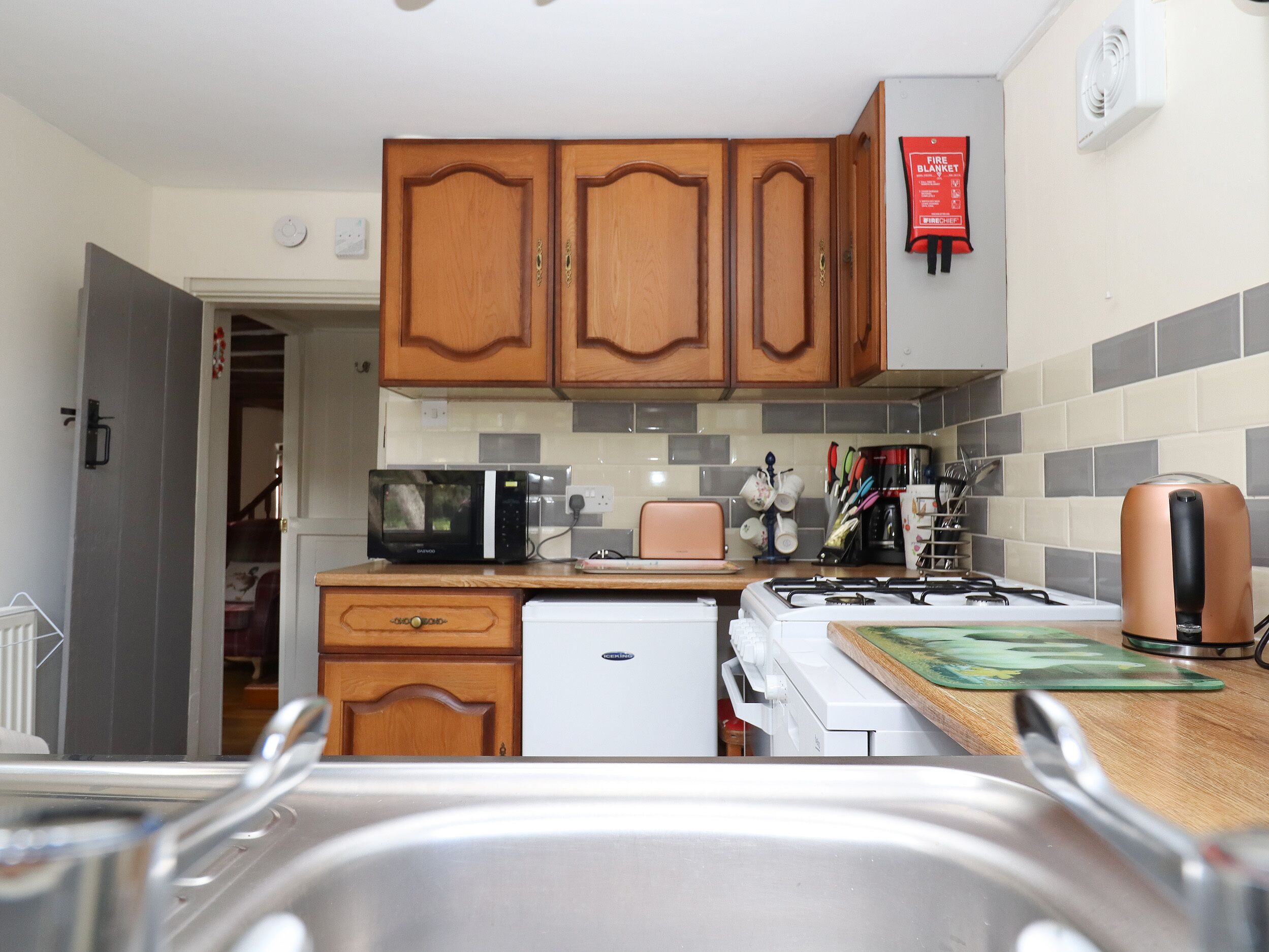 Een kleine keuken met houten kastjes, een magnetron, een broodrooster en een gasfornuis.