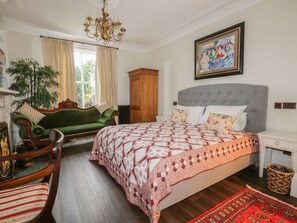 A bedroom with a large bed, a green sofa, a wooden cabinet, and a painting on the wall. - Ash Tree Lodge (Hull)