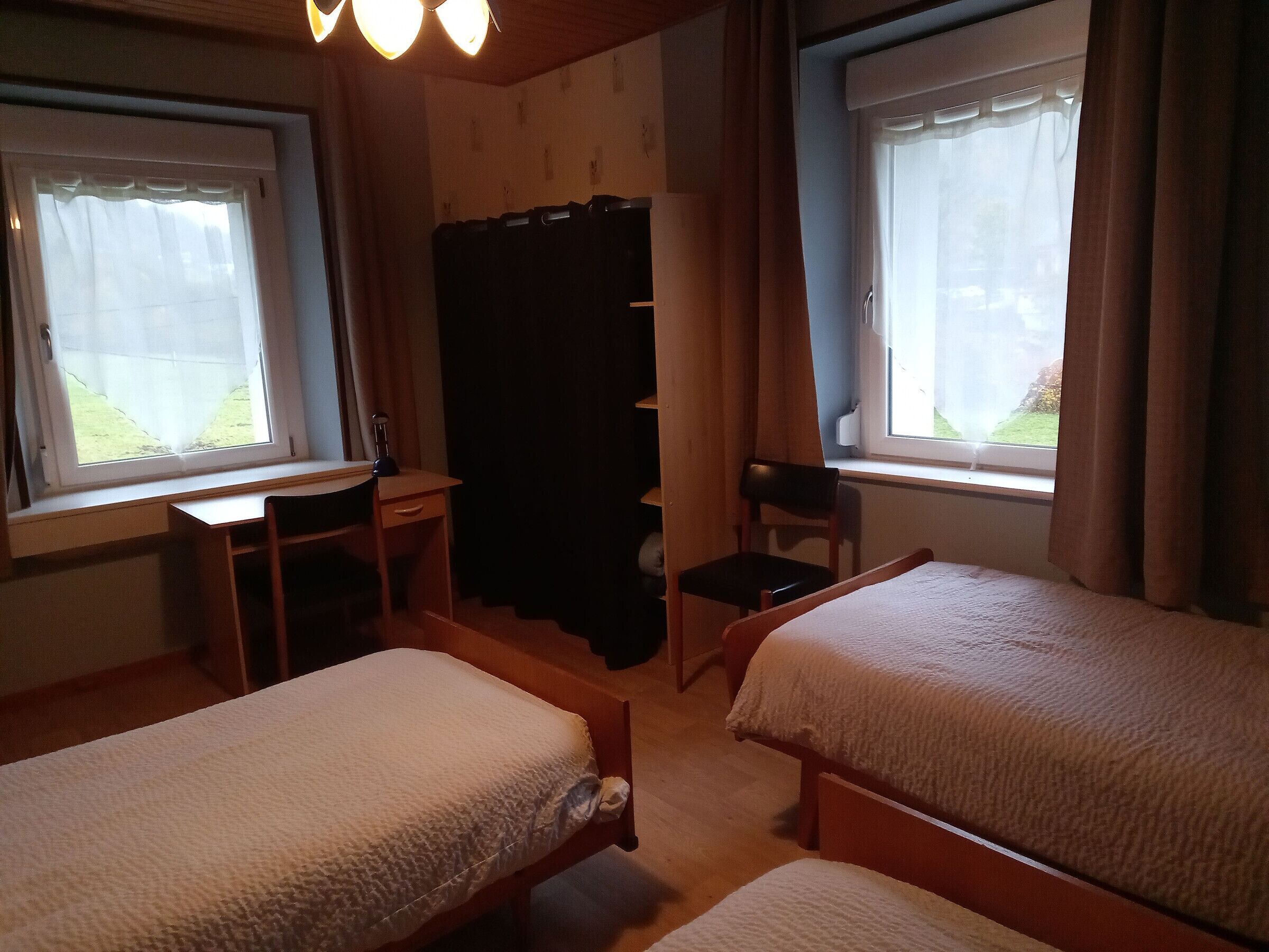 A bedroom with two beds, a desk, a chair, and a window.
