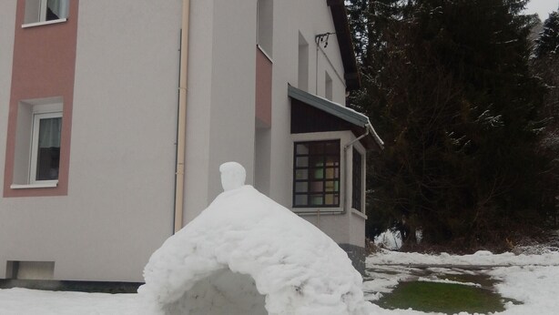 A snowman with a chimney, a house in the background, and a snowy landscape.