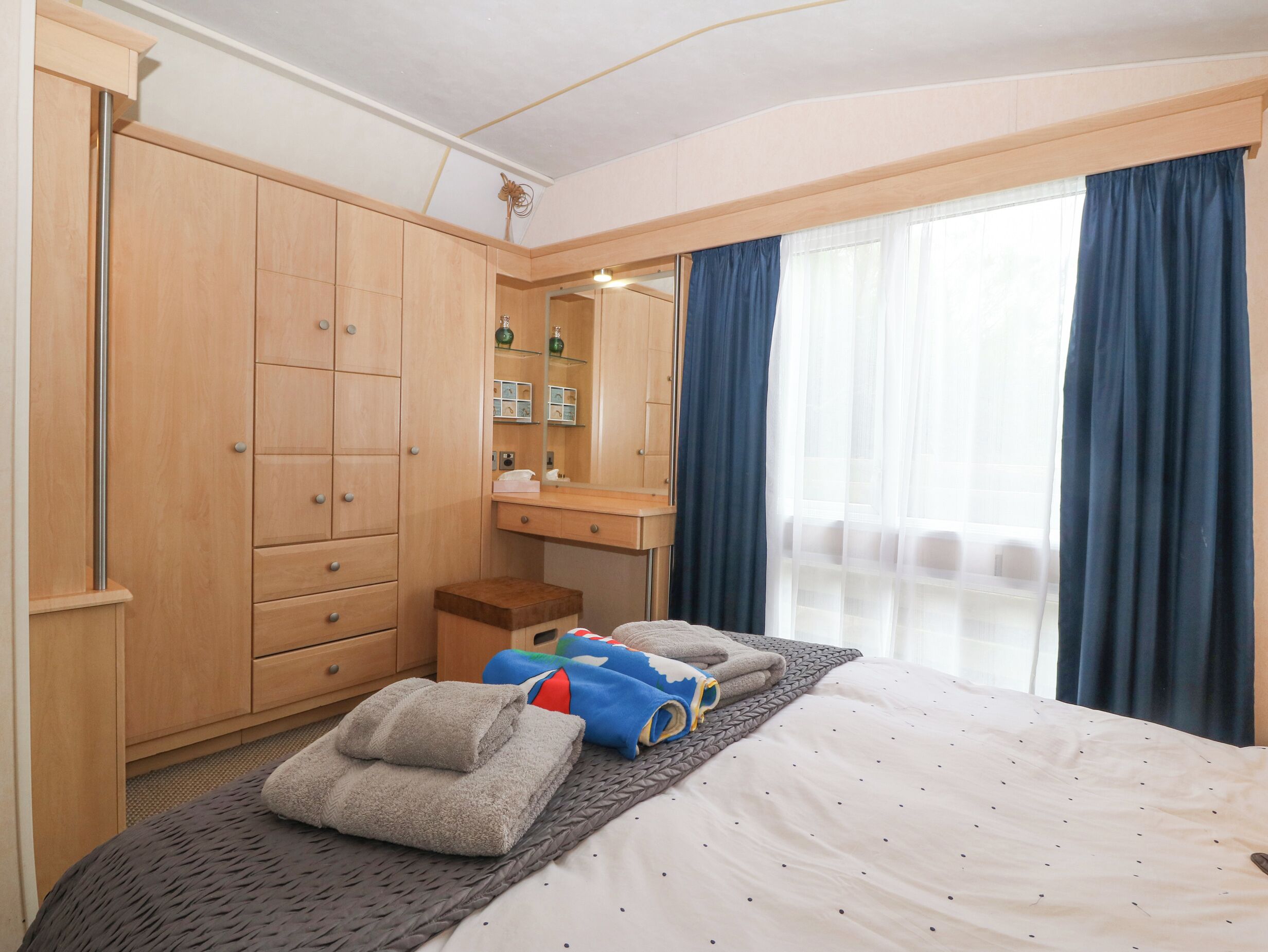 A hotel room with a bed, a wooden wardrobe, a small table, and a mirror.