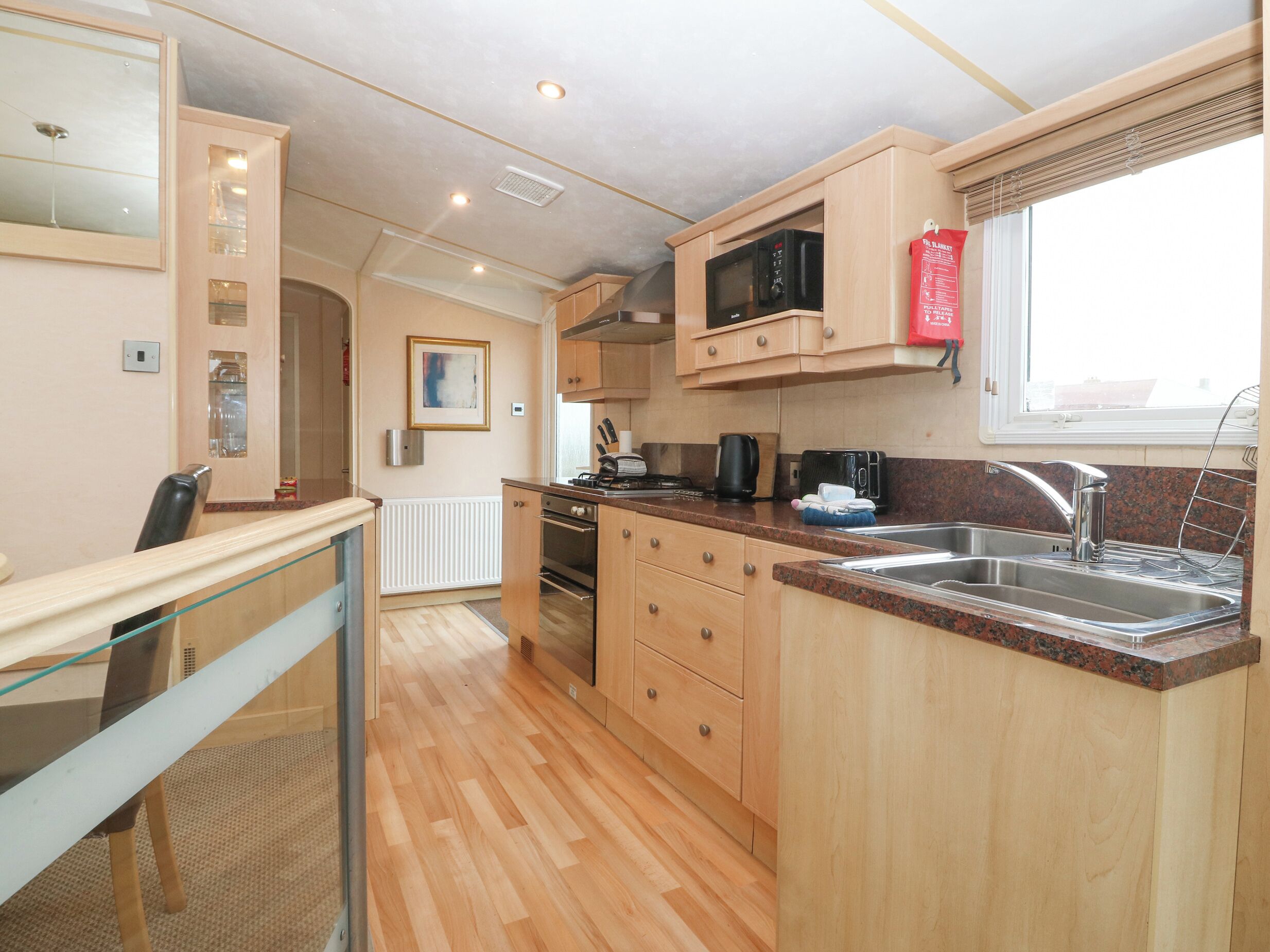 Una cocina compacta con armarios de madera, un microondas, un hervidor y un lavabo.