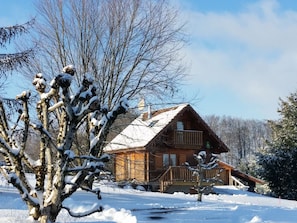 A wooden cabin with a balcony, surrounded by snow-covered trees.