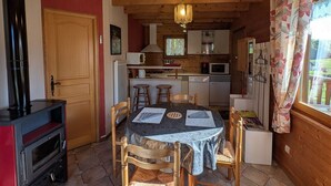A cozy cabin interior with a dining area, kitchen, and a wood stove. - Cozy Chalet near Plombières-les-Bains - Ideal for Couples, Nature Trails, and Relaxing Spa Retreat (Le Val-d'Ajol)