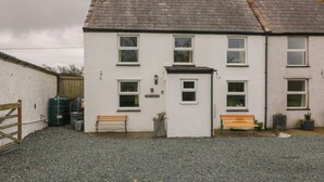 A two-story white building with a grey tiled roof, a small front porch, and two benches. - Bron Gadair (Llanfairpwllgwyngyll)