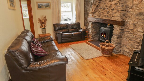 A cozy living room with a stone fireplace, leather sofas, and wooden flooring. - Bron Gadair (Llanfairpwllgwyngyll)