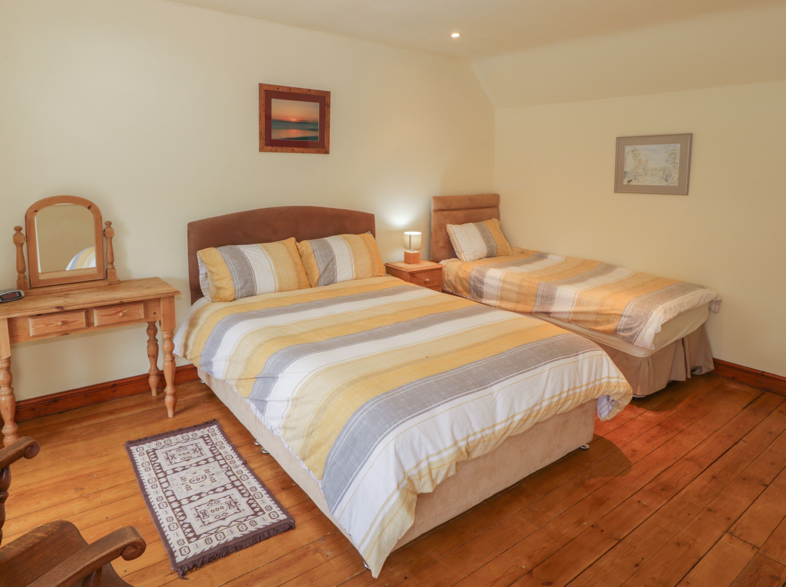 A bedroom with two beds, a wooden dresser, a mirror, and a rug.