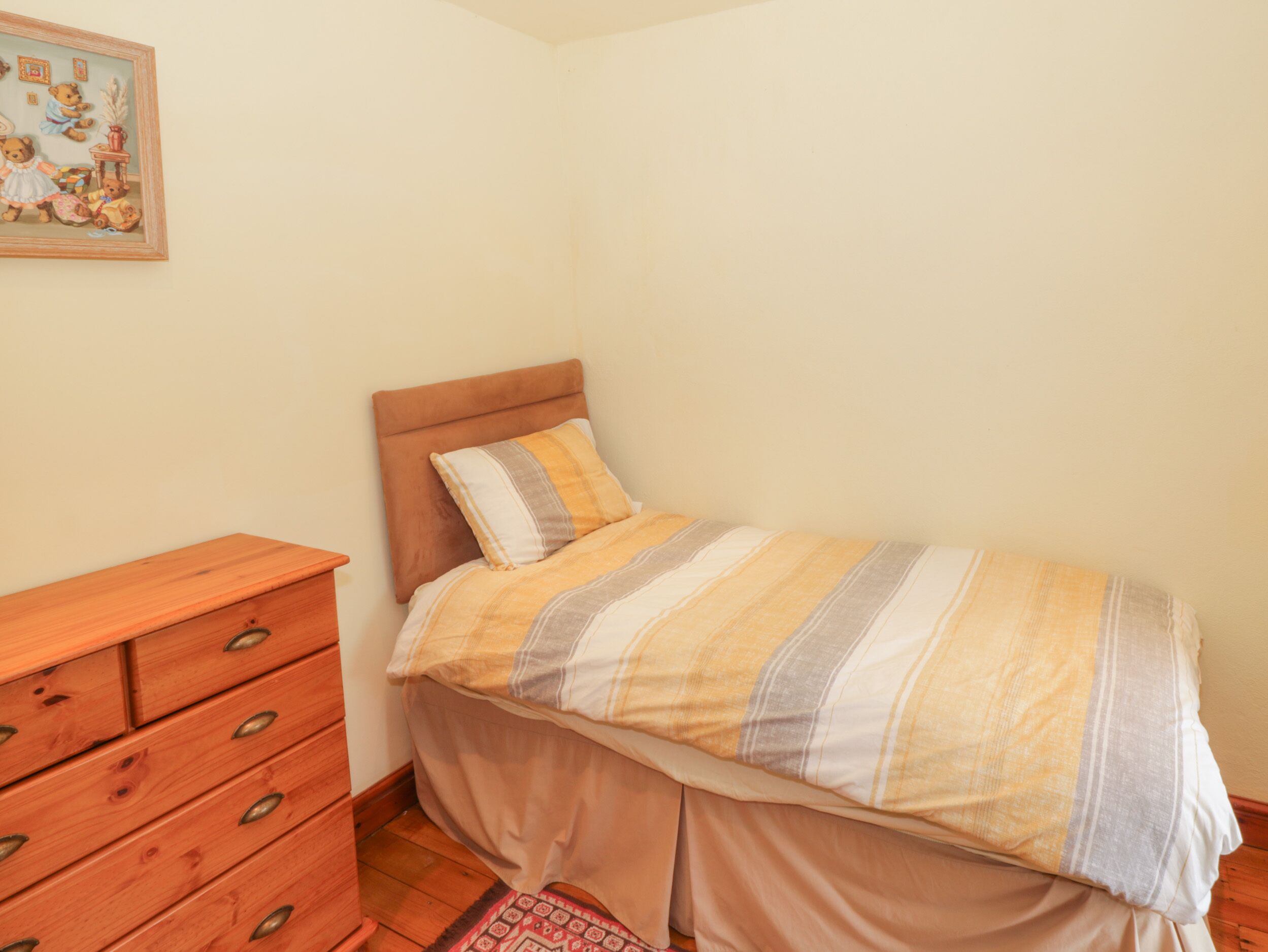 A bedroom with a bed, wooden dresser, and a wall painting.