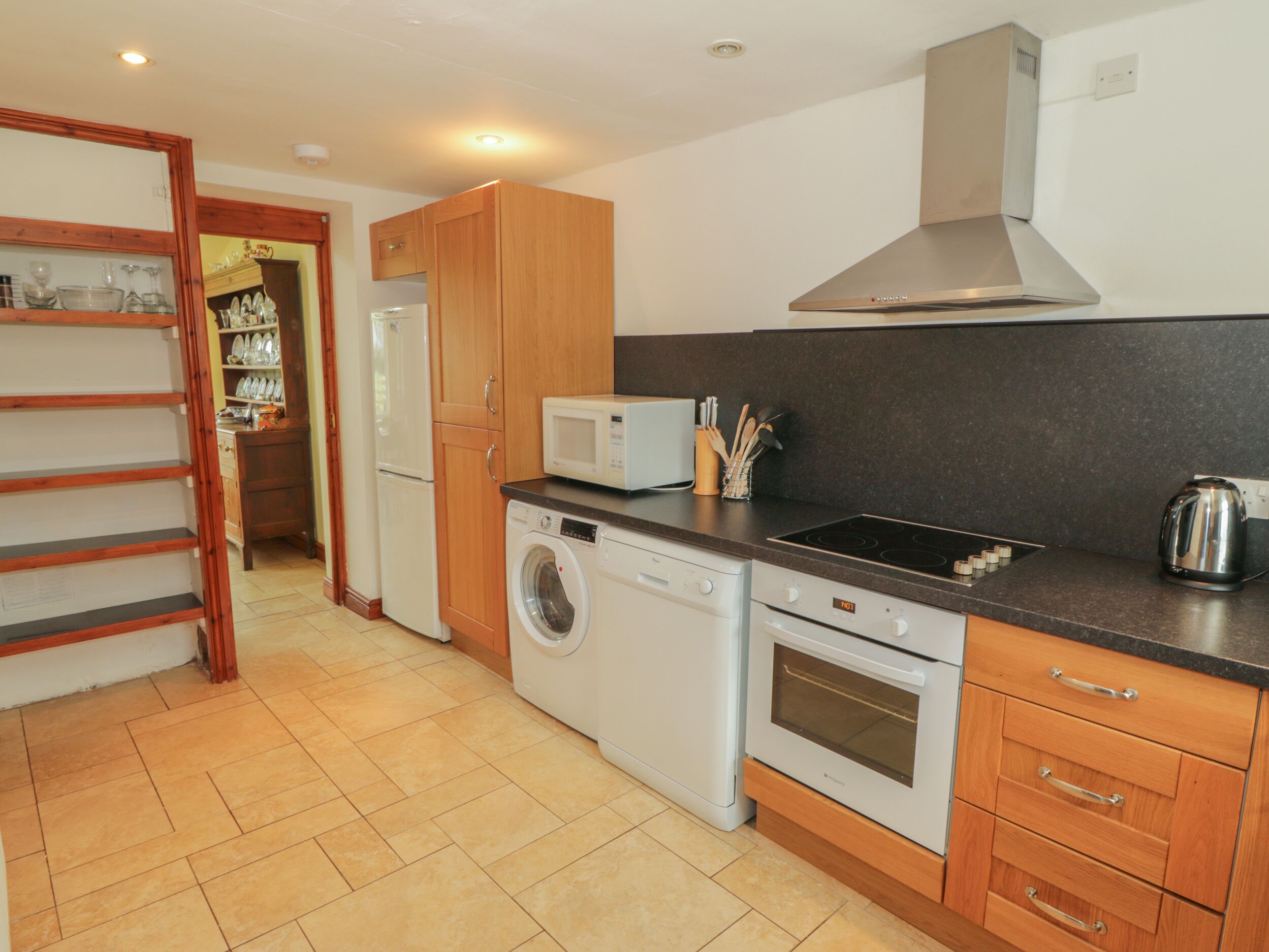 A compact kitchen with a washing machine, oven, microwave, and a stainless steel range hood.