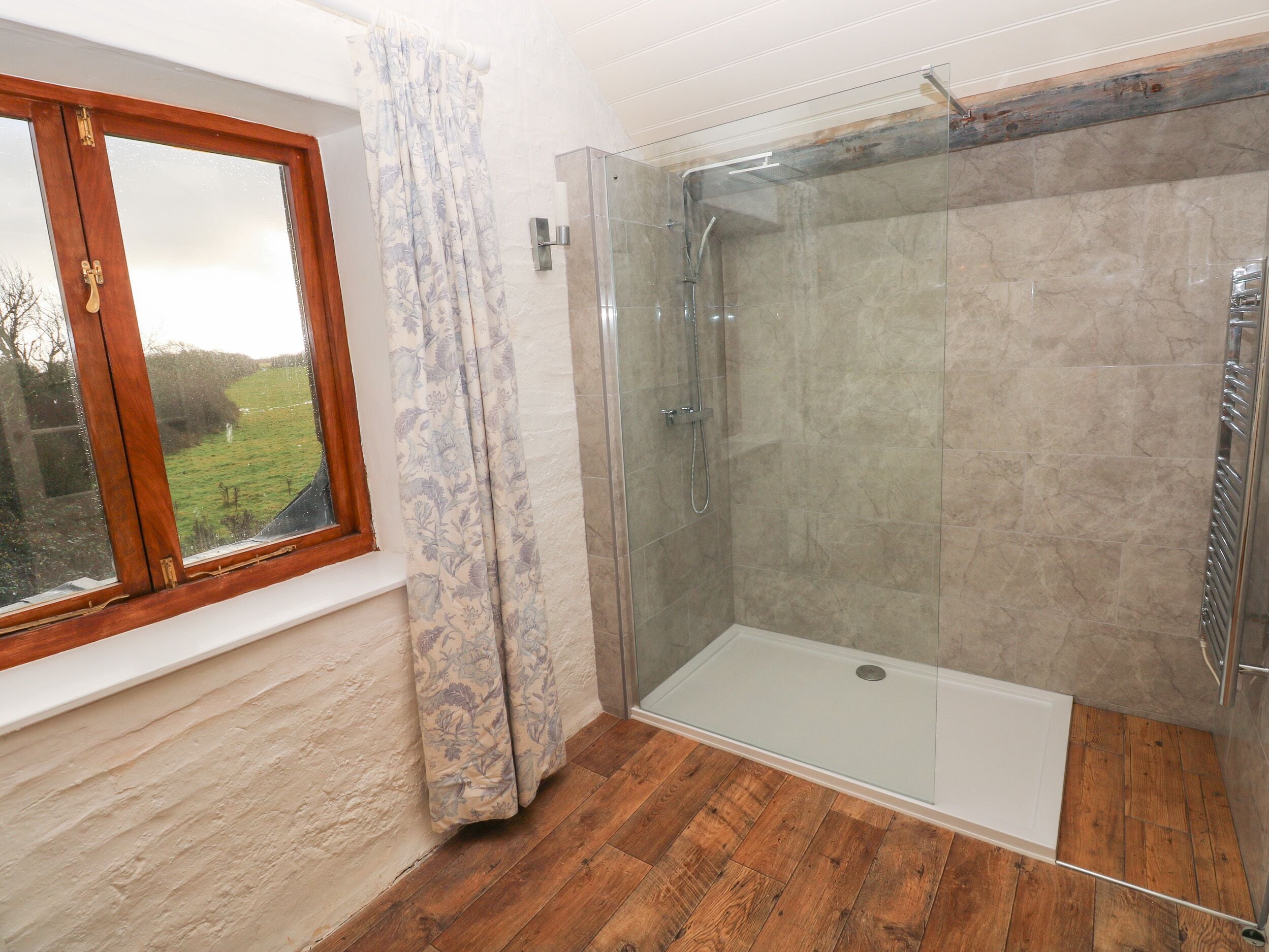 A shower room with a glass door, a window with a wooden frame, and a curtain.