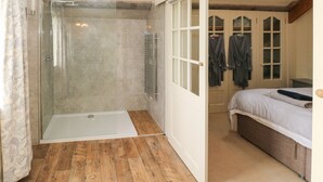 Een badkamer met een douche in een glazen cabine, een witte badkuip, houten vloeren en een bed met een witte matras.