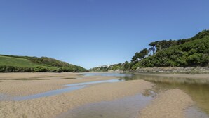 Une rive de rivière bordée d’eau claire, de plages de sable et, au loin, de collines verdoyantes.