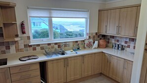 Une cuisine avec des meubles de rangement en bois, une fenêtre donnant sur un beau paysage, un évier et un appareil à faire du pain.
