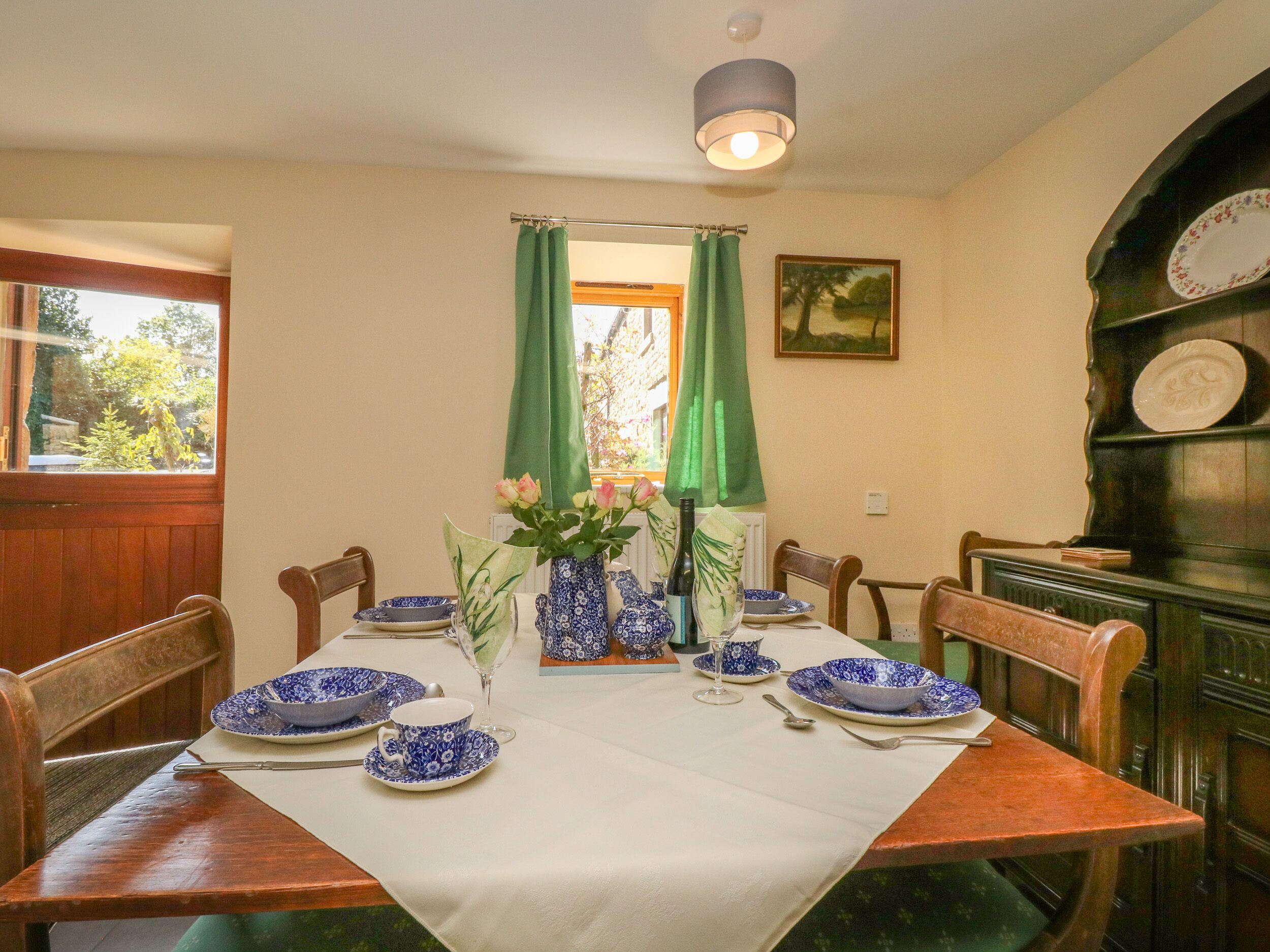 A dining room with a table set for four, featuring blue and white patterned tableware, a vase with flowers, and a green curtain.