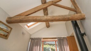 A room with exposed wooden beams, a skylight, a window with curtains, and a black pipe. - The Old Cart House (Hope Valley)