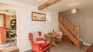 A cozy living room with a red armchair, a small round table with a bottle and fruit, and a staircase with wooden railings. - The Old Cart House (Hope Valley)