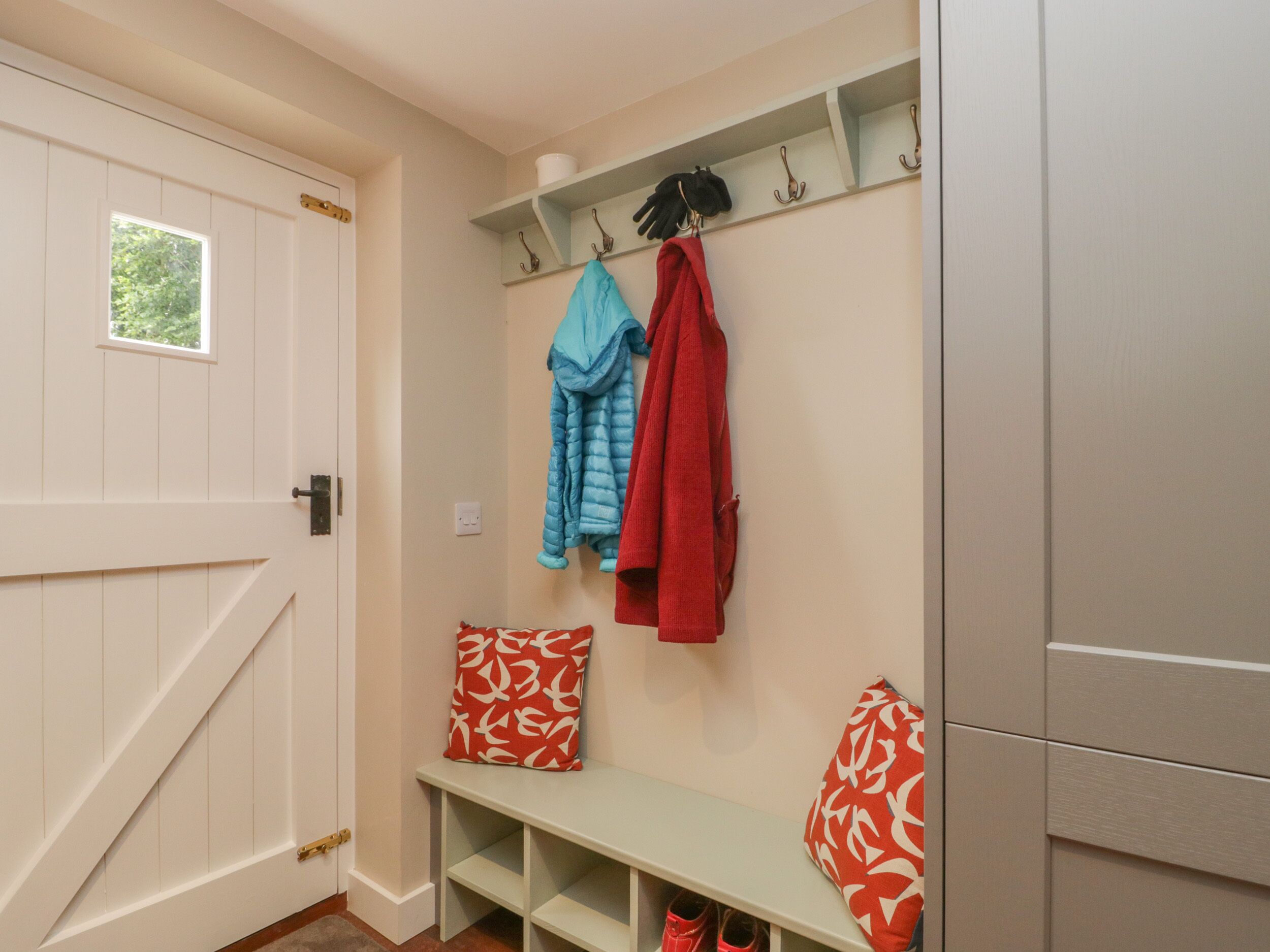 A hallway with a bench, a coat rack with jackets, and a door.