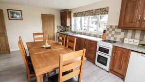 A compact kitchen with wooden cabinets, a granite countertop, a built-in oven, and a dining area with a wooden table and chairs. - Sandmartins (Chester)