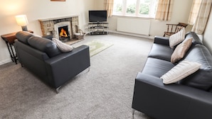 A living room with two black sofas, a fireplace, a TV, and a window with curtains. - Sandmartins (Chester)