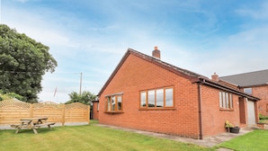 A single-story brick house with a sloped roof, a front door, and a visible chimney. - Sandmartins (Chester)