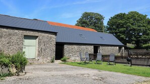 A stone building with a sloped roof, a green door, and a small porch area with chairs. - Dale Barton (Wells)