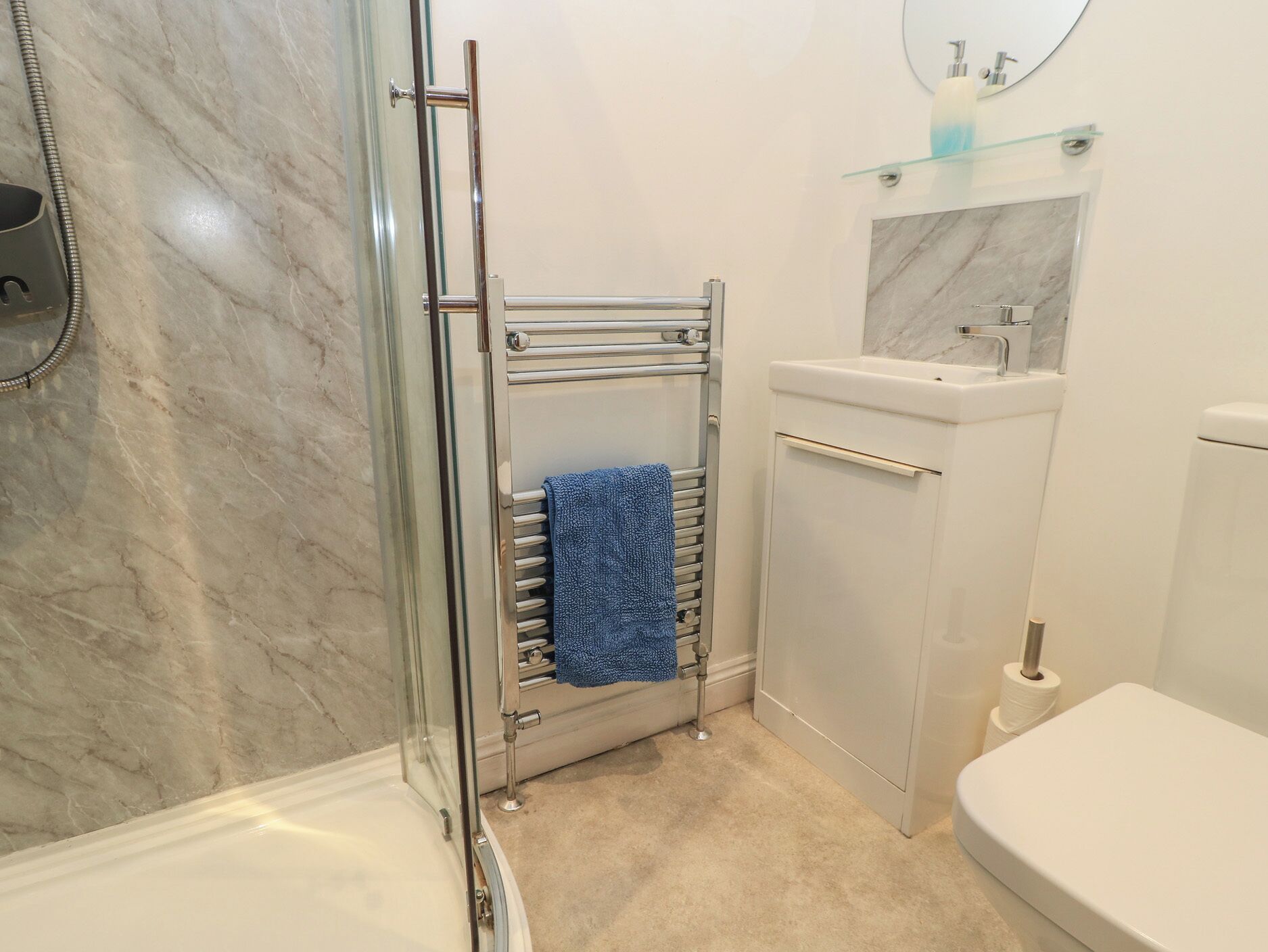 A bathroom with a glass shower enclosure, a towel rack with a blue towel, a marble-topped sink, and a toilet.