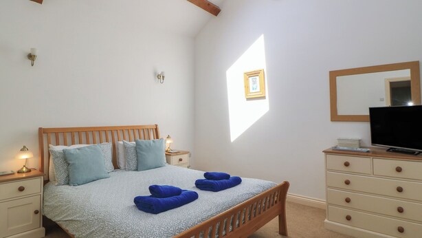A bedroom with a wooden bed, bedside tables, a dresser, a TV, and a skylight. - Dale Barton (Wells)
