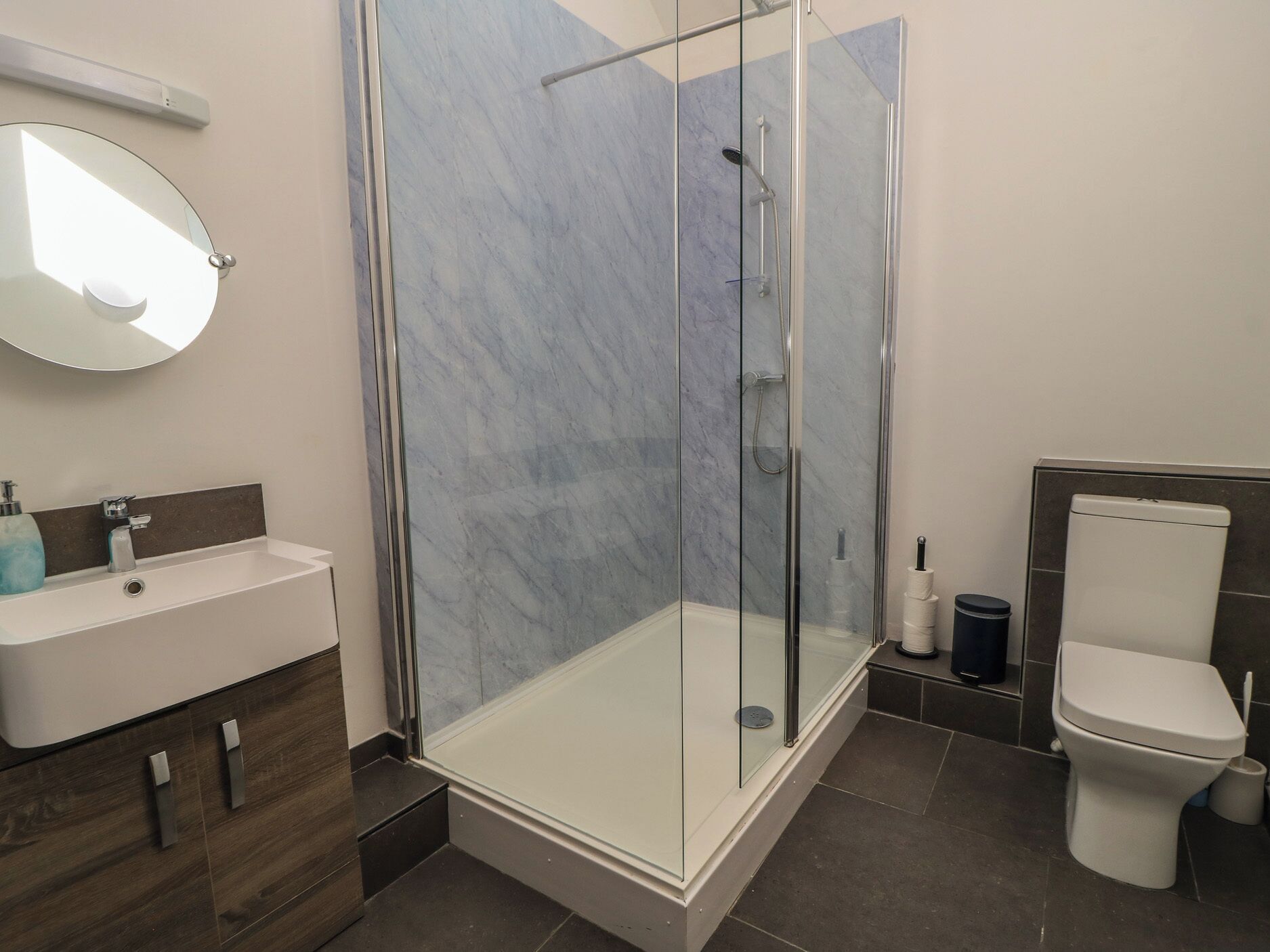 A modern bathroom with a glass-enclosed shower, a sink with a mirror, and a toilet.