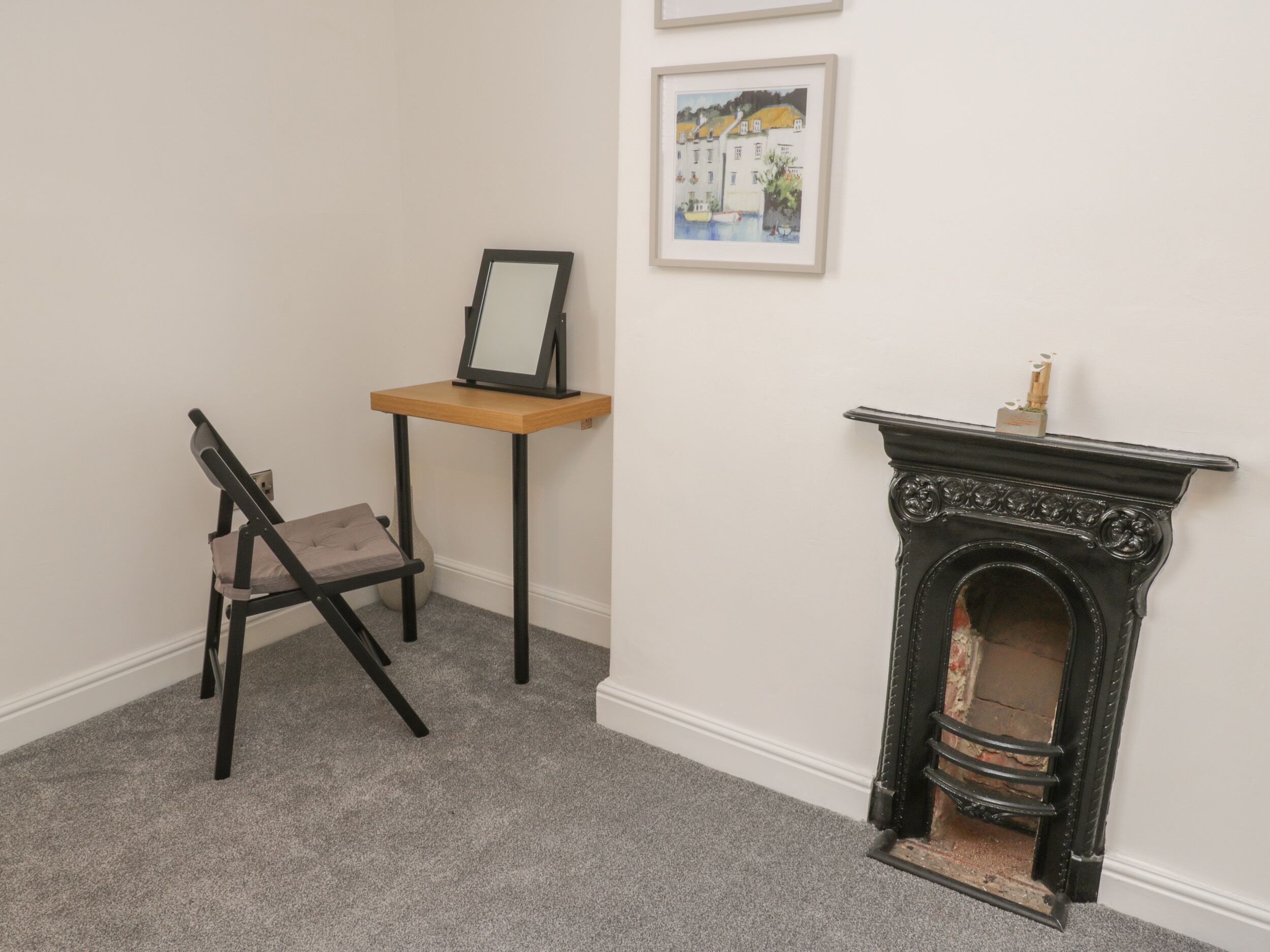 A room with a fireplace, a chair, a small table with a picture frame, and a painting on the wall.