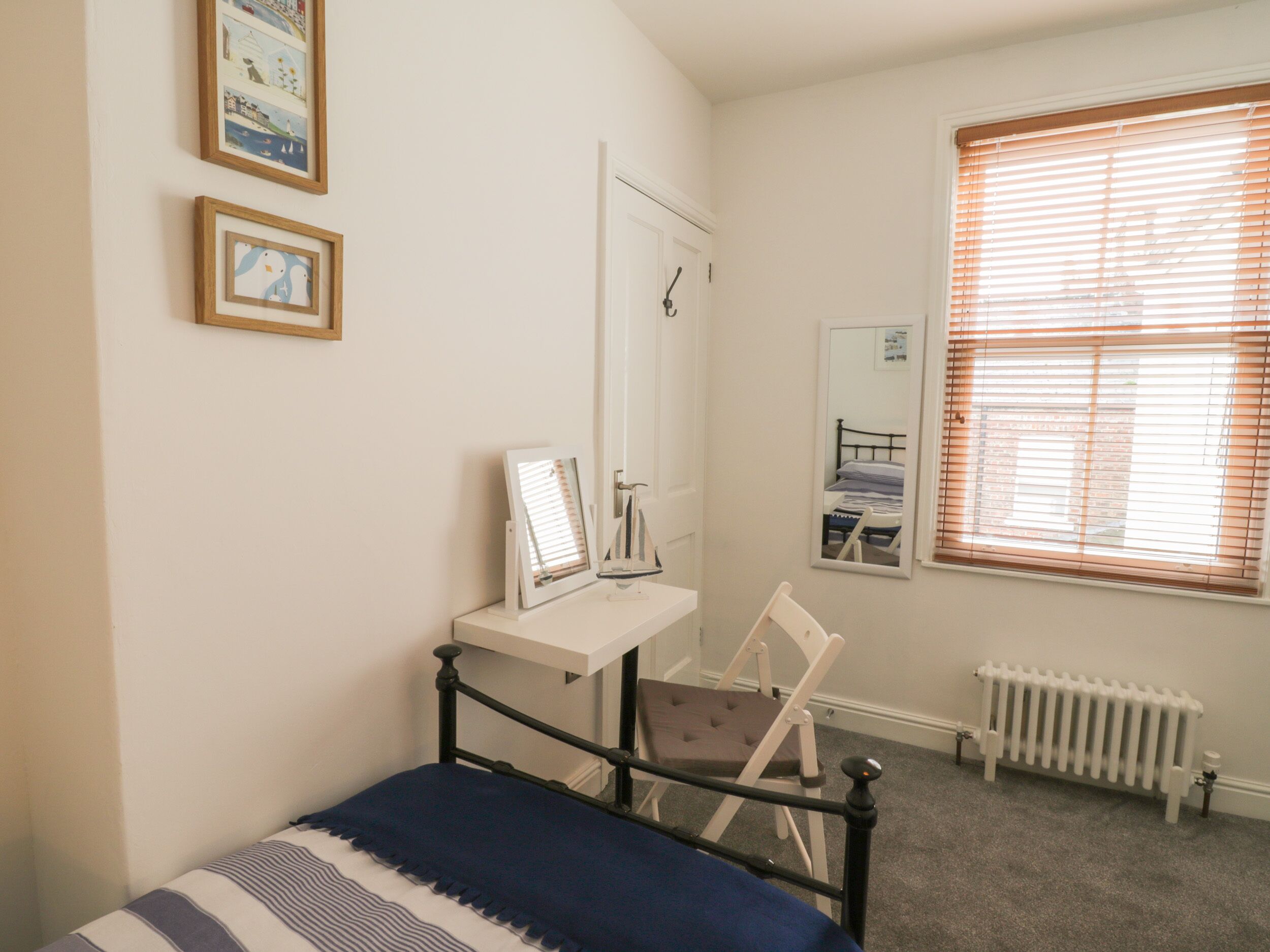 A bedroom with a bed, a desk, a chair, a radiator, and a window with blinds.