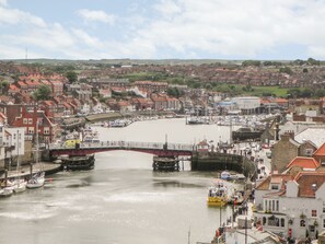 A harbor with boats, a bridge, and buildings with red roofs. - Laridae (Whitby)