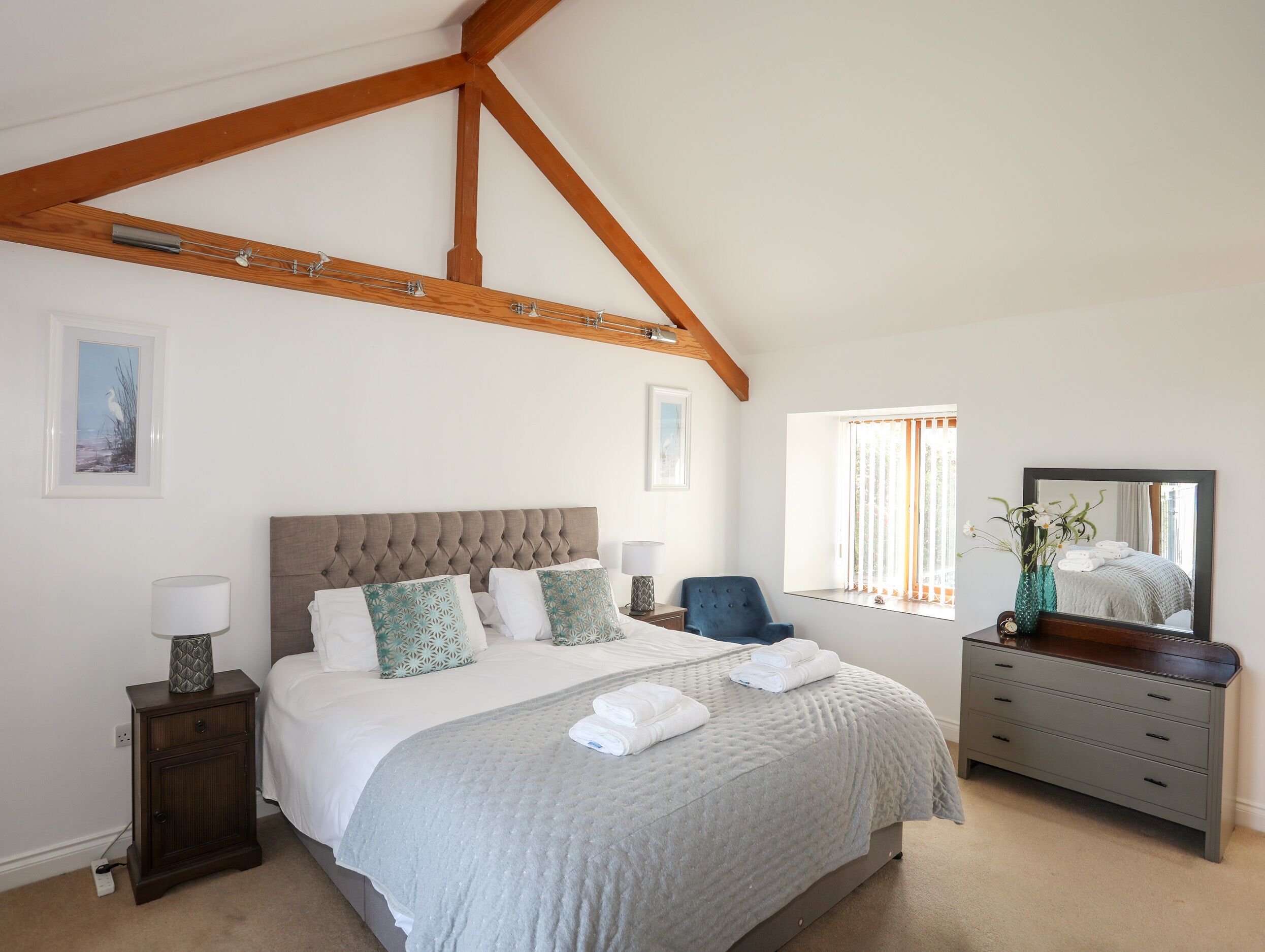 A bedroom with a large bed, a nightstand, a dresser, and a window with curtains.